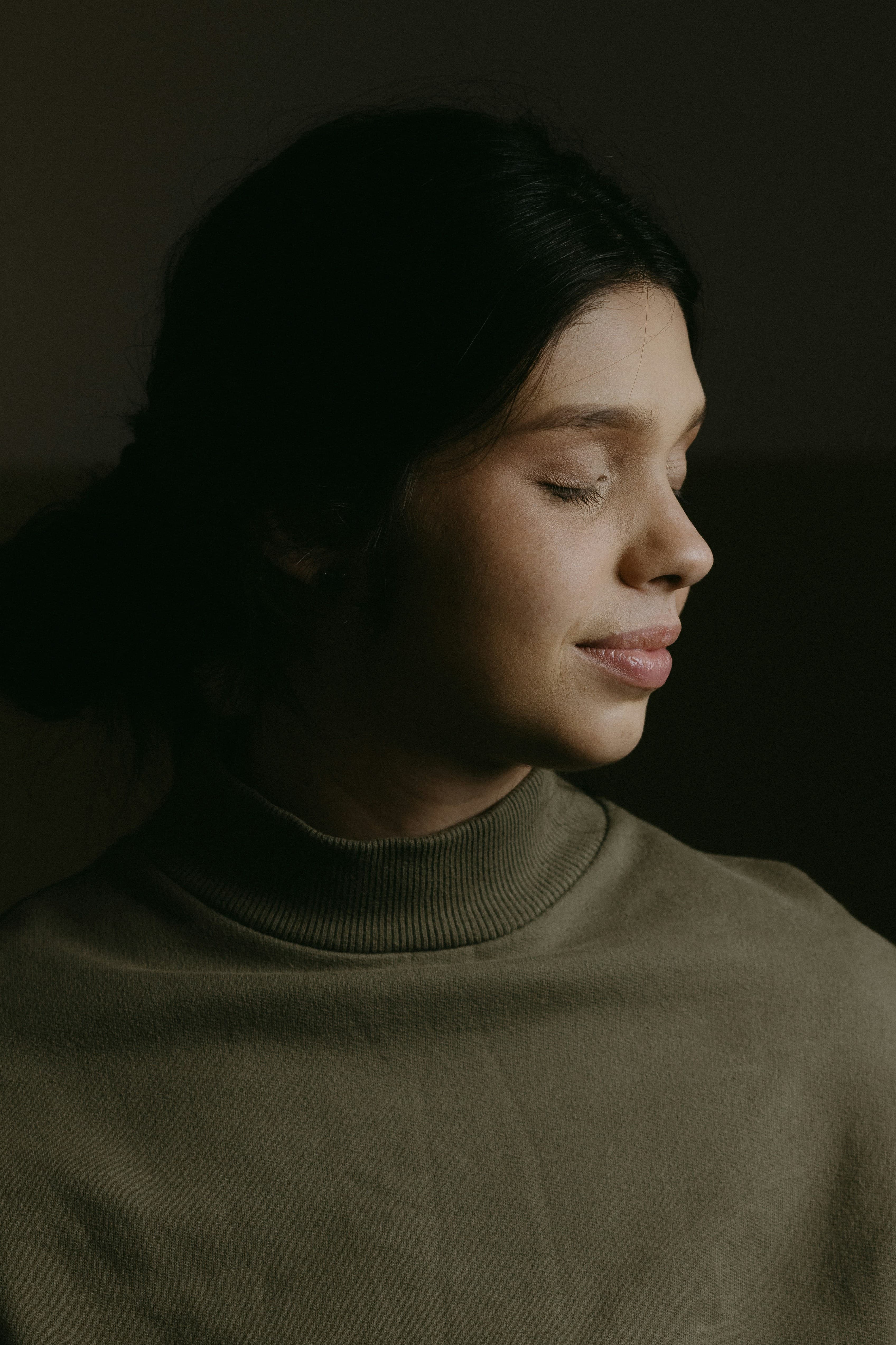 Serene woman with closed eyes in black turtleneck against dark background, embodying peaceful confidence and intentional presence